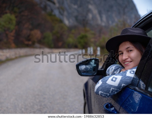 Asian young hipster woman traveling on\
car vacation. Autumn drive. The rain is falling. The concept of\
freedom of movement. Fall weekend in the\
mountains.