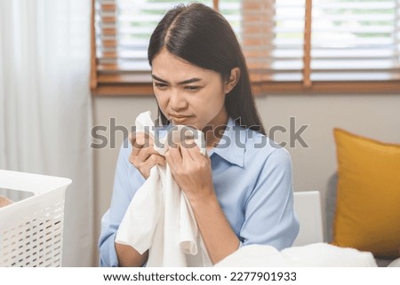 Asian young housewife woman, girl expression face bad smelling clothes, sniff smelly dirty stinky musty, look disgusting from clothes after washed clothes, laundry out of machine in room at home.