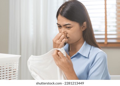 Asian young housewife woman having bad smelling clothes holding breath nose with fingers, sniff smelly dirty stinky musty, look disgusting from clothes after washed clothes, laundry out of machine. - Shutterstock ID 2281213449