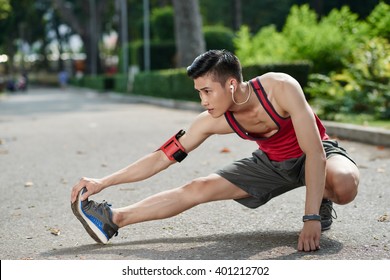 Asian Young Jogger Stretching Legs Outdoors