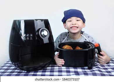 An Asian Young Kid Boy Cooking His Croissant For The Breakfast By Using A Black Oil-free Air Fryer In The Kitchen With White Cement Wall Background