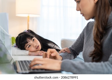 Asian Young Kid Daughter Feeling Sad And Need To Play With Busy Mother. Attractive Beautiful Mom Use Laptop Computer Working From Home During New Normal And Have No Time For Little Child Girl In House