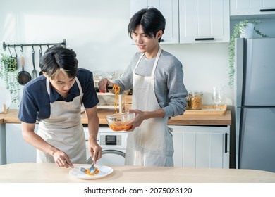 Asian Young LGBTQ Male Gay Family Enjoy Cook Foods In Kitchen At Home. Attractive Handsome Romantic Man Couple Wear Apron Feeling Happy And Cheerful To Spending Time Making Spaghetti Together In House