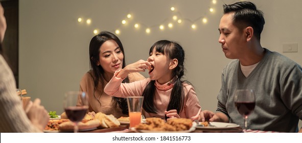 Asian Young Little Girl Enjoy Eating Her Meal Crispy Fried Chicken Together With Family In Christmas And New Year Party. The Kid Feeling Happy To Stay With Parents And Grandparents During Holiday.