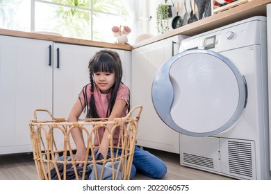 Asian Young Little Kid Put Dirty Clothes Into Washing Machine In House. Lovely Girl Child Sit On Floor, Feel Happy To Help Family And Loads Laundry In Washer Appliance At Home. Domestic-House Keeping.
