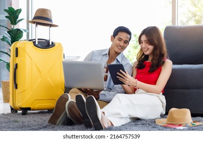 Asian young lovely boyfriend and girlfriend traveler couple sitting smiling on carpet in living room with trolley luggage while using laptop computer and tablet booking vacation summer trip online. - Shutterstock ID 2164757539