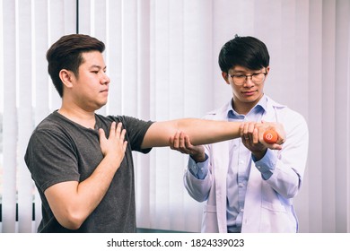 Asian Young Male Physiotherapist Helping Patient With Lifting Dumbbells Exercises In Clinic.