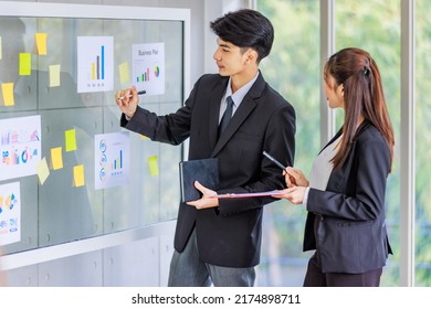 Asian young male professional successful businessman manager pointing paperwork company target graph chart diagram document on glass board explaining to female secretary employee staff in formal suit. - Shutterstock ID 2174898711