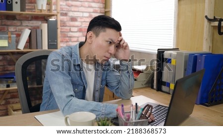 asian young male is propping his head and staring at the monitor while pondering on a difficult project on the computer in the office.