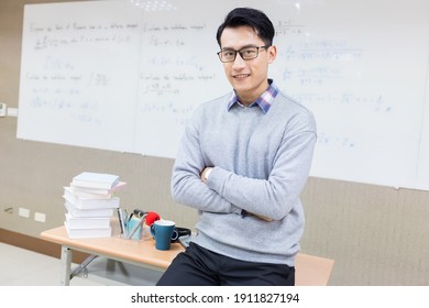 asian young male teacher smiles at you with cross arm in classroom