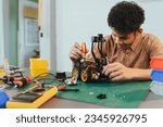 Asian young man assembling a robotic car, focus on robotics, assembling a robotic robot to develop intelligent robotics, mechanics students assembling a rescue robot car. Surveillance Robot.