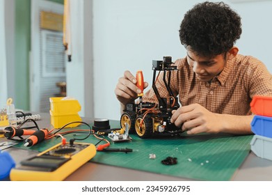 Asian young man assembling a robotic car, focus on robotics, assembling a robotic robot to develop intelligent robotics, mechanics students assembling a rescue robot car. Surveillance Robot.