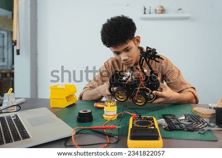 Asian young man assembling a robotic car, focus on robotics, assembling a robotic robot to develop intelligent robotics, mechanics students assembling a rescue robot car. Surveillance Robot.