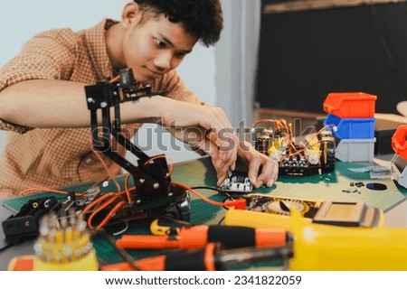 Asian young man assembling a robotic car, focus on robotics, assembling a robotic robot to develop intelligent robotics, mechanics students assembling a rescue robot car. Surveillance Robot.