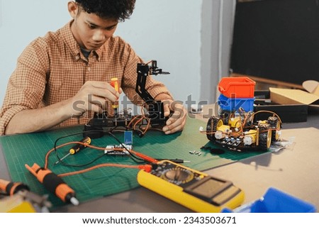 Asian young man assembling a robotic car, focus on robotics, assembling a robotic robot to develop intelligent robotics, mechanics students assembling a rescue robot car. Surveillance Robot.