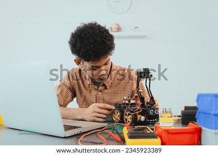 Asian young man assembling a robotic car, focus on robotics, assembling a robotic robot to develop intelligent robotics, mechanics students assembling a rescue robot car. Surveillance Robot.