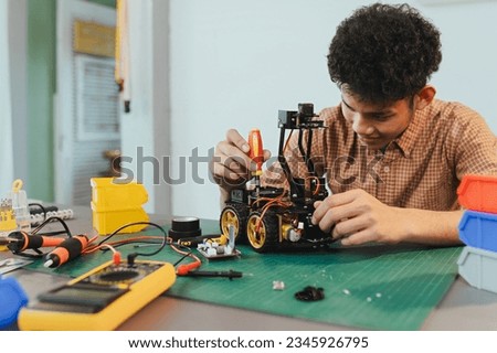 Asian young man assembling a robotic car, focus on robotics, assembling a robotic robot to develop intelligent robotics, mechanics students assembling a rescue robot car. Surveillance Robot.