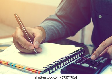 Asian Young Man Doing Finances With Using Calculator And Writing Note In Home Office.