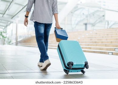 Asian young man dragging a suitcase along the city or airport terminal with shopping bags. Man traveling in the city or urban area.