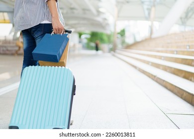 Asian young man dragging a suitcase along the city or airport terminal with shopping bags. Man traveling in the city or urban area.