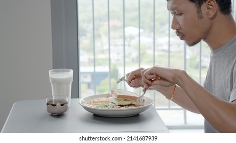 Asian Young Man Eating Breakfast At The Dining Room Table Full Of Food, He Lifted Up The Milk And Drank It, Refreshed.