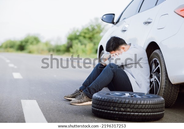 Asian young man\
failed to fix a problem on the road, Car broke down or changing\
flat tire on the road\
concept.