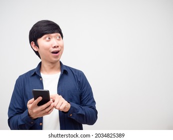 Asian Young Man Holding And Press Mobile Phone In His Hand Feeling Excited And Lookign At Copy Space White Isolated