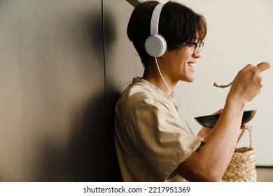 Asian young man listening to music and eating food while sitting on floor at home - Powered by Shutterstock