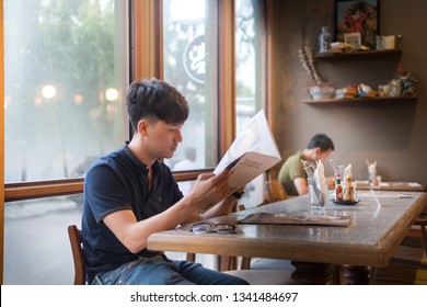 Asian Young Man Looking At The Menu In A Restaurant.