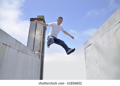 Asian Young Man Making A Giant Leap In Between Buildings