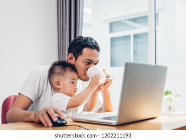 Asian Young Man Parent, Father Using Working On Laptop Computer With Baby Son At Home Office, And He Son Helped To Give Coffee To The Dad For Drink, Work From Home Concept