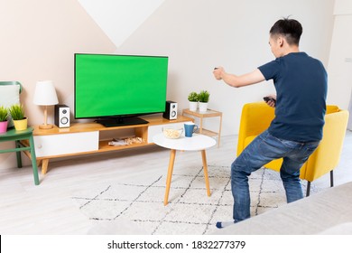 asian young man is playing and winning motion sensing game on a green chroma key TV screen and shake his arm at home - Powered by Shutterstock