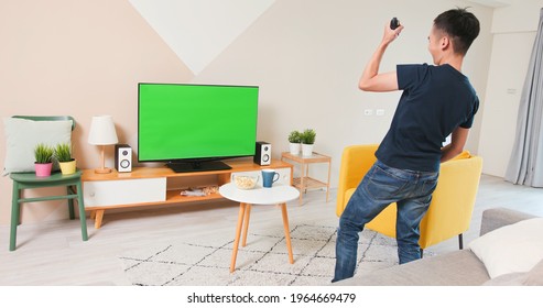 asian young man is playing and winning motion sensing game on a green chroma key TV screen and shake his arm at home - Powered by Shutterstock