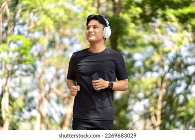 Asian young man running at the park in the morning. He listens to his favorite music with wireless headphones. - Powered by Shutterstock