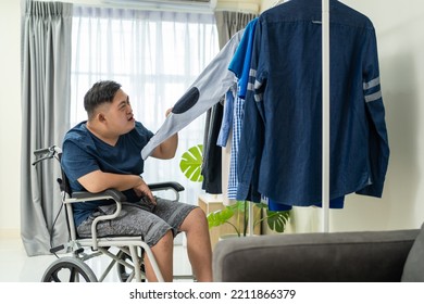 Asian Young Man Sit On Wheelchair And Choosing Clothes On Closet Rack. Attractive Male Patient Person Feeling Happy And Relax, Then Getting Dressed In Bedroom For Morning Lifestyles At House.