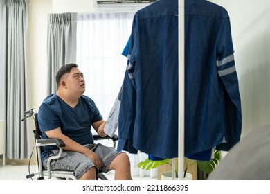 Asian Young Man Sit On Wheelchair And Choosing Clothes On Closet Rack. Attractive Male Patient Person Feeling Happy And Relax, Then Getting Dressed In Bedroom For Morning Lifestyles At House.