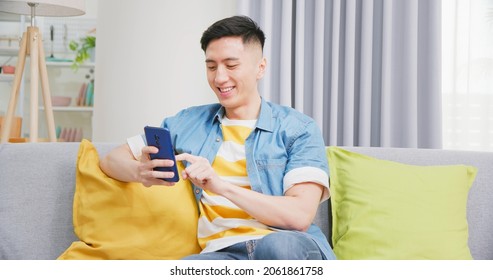 asian young man sitting on sofa check social media by mobile phone happily in living room at home - Shutterstock ID 2061861758