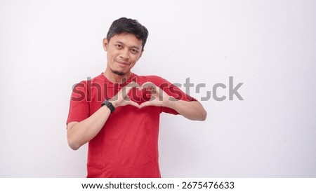 Asian young man smiling while giving heart shape symbol using fingers on white background. studio shot