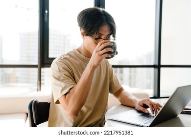 Asian Young Man Studying With Laptop Computer While Sitting By Table In Bright Room At Home