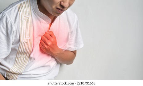 Asian Young Man Suffering From Central Chest Pain. Chest Pain Can Be Caused By Heart Attack, Myocardial Infarct Or Ischemia, Myocarditis, Pneumonia, Oesophagitis, Stress, Anxiety, Etc,.