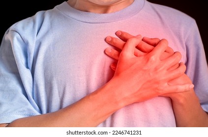 Asian young man suffering from left lateral chest pain. Chest pain can be caused by heart attack, myocardial infarct or ischemia, myocarditis, pneumonia, oesophagitis, stress, anxiety, etc,.