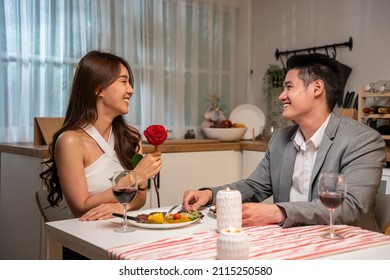 Asian young man surprise and give rose flower to beautiful girlfriend. Attractive romantic new marriage couple man and woman having dinner together to celebrate anniversary and valentines day in house