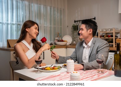 Asian Young Man Surprise And Give Rose Flower To Beautiful Girlfriend. Attractive Romantic New Marriage Couple Man And Woman Having Dinner Together To Celebrate Anniversary And Valentines Day In House