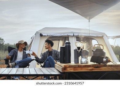 Asian young man two persons sitting enjoy coffee drink near a camping tent in the morning time, coffee drink relaxing on the morning summer camping vacation. - Powered by Shutterstock