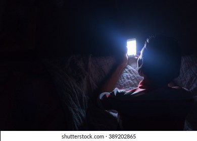 Asian young man using his mobile phone on the bed in dark room.
Thin guy playing his smartphone on the bed in dark room.