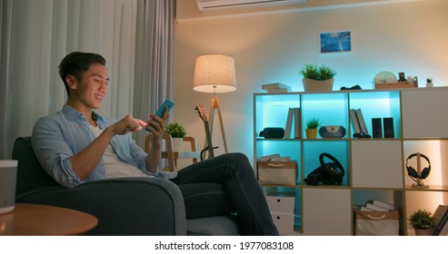 Asian Young Man Using Smart Home App To Control Light Colors In The Evening At Home