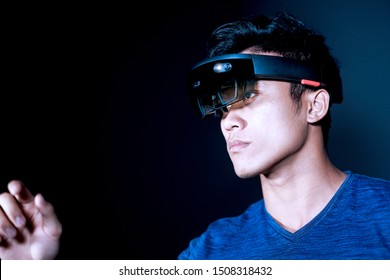 The Asian young man with virtual reality glasses experiences VR hololens headset in studio with advanced technology. Mixed reality concept of the future.