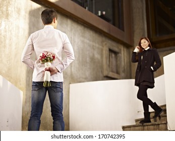 Asian Young Man Waiting By The Steps With Flowers Behind Back For His Girlfriend.