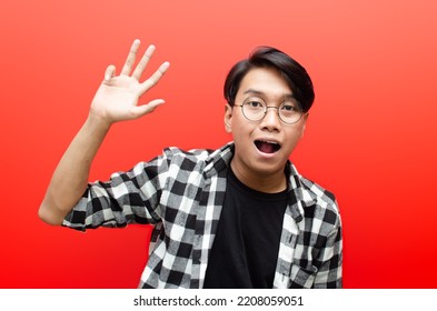 Asian Young Man Waving Hand Saying Hello, Hi, Good Bye With Smiling Happily Expression Isolated Over Red Background. Billboard Advertisment Model Concept.