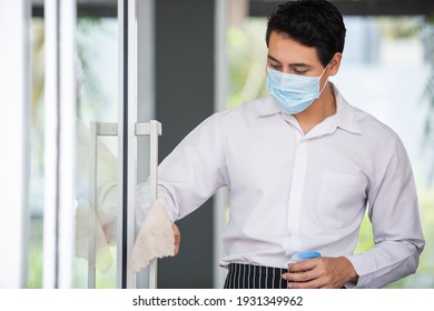 Asian Young Man Wear Face Mask White Shirt Wipe Cleaning Window Glass With Spray Alcohol For Sterilize In Restaurant. Employee Cleaning At Workplace.